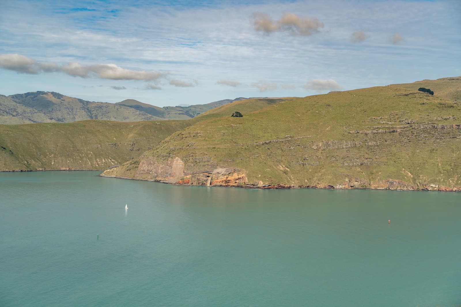 Calm sea-glass green harbour beneath golden hills — home water for harbourside hospitality